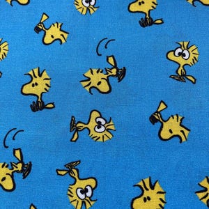 Könnte beinhalten: Ein blauer Stoff mit einem sich wiederholenden Muster aus gelben Comic-Vögeln. Die Vögel haben schwarze Augen und Schnäbel und befinden sich in verschiedenen Posen.