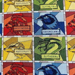 Op de afbeelding: Een kleurrijke stof met een herhalend patroon van glas-in-loodramen met de wapenschilden van de Hogwarts-huizen. De wapenschilden omvatten Griffoendor, Huffelpuf, Zwadderich en Ravenklauw. Elk wapenschild is omgeven door een kleurrijke glas-in-loodrand.
