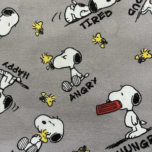 May include: Gray fabric featuring a repeating pattern of Snoopy in various poses with words like "Love", "Tired", "Angry", and "Hungry". Yellow Woodstock birds are also scattered throughout the design.