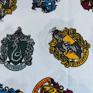 May include: White fabric with a repeating pattern of four Hogwarts house crests. The crests are in their traditional colors: Gryffindor (red and gold), Hufflepuff (yellow and black), Slytherin (green and silver), and Ravenclaw (blue and bronze).