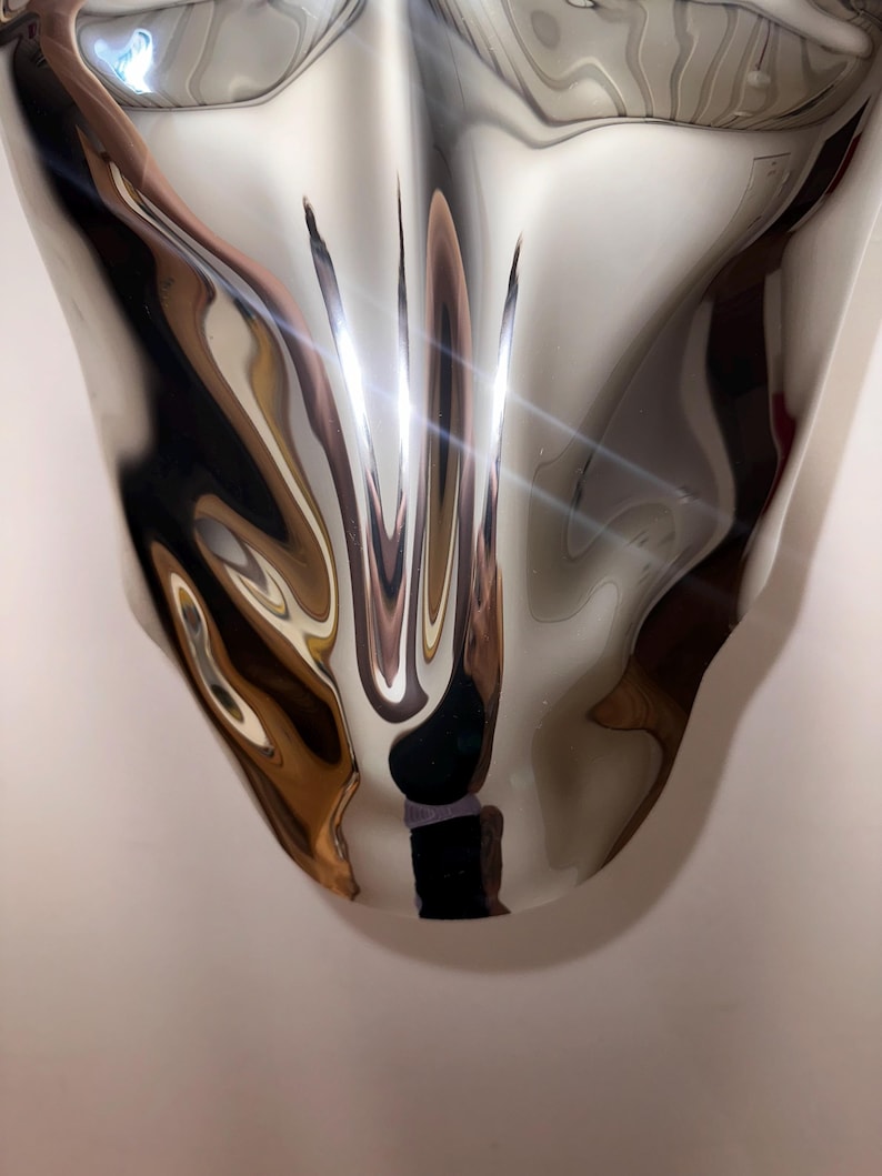 May include: A silver, abstract, metallic sculpture with a smooth, reflective surface. The sculpture is shaped like a teardrop and has a distorted, wavy appearance.