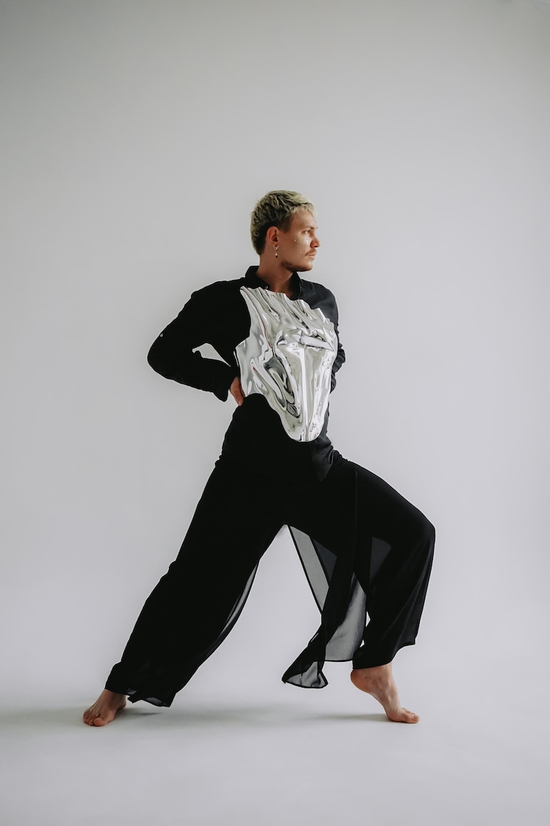 May include: A person wearing a black shirt and pants with a silver metallic corset. The person is standing with one leg forward and is looking to the right.