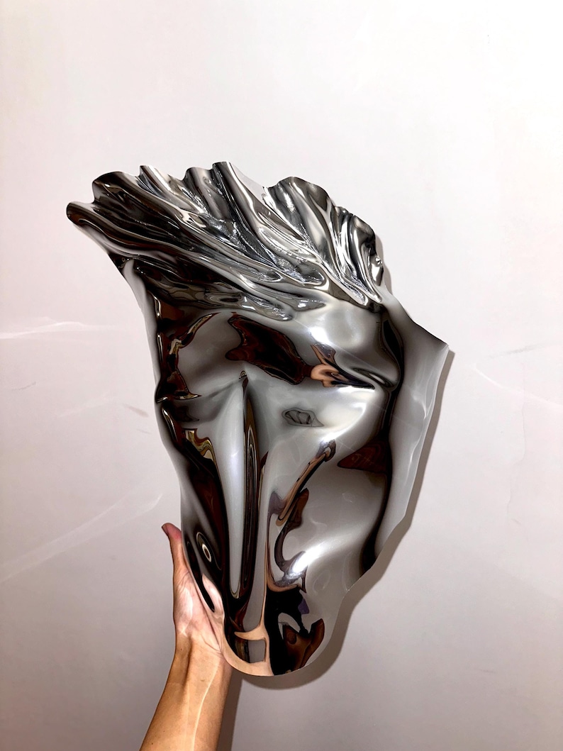 May include: A silver metal vase with a unique, abstract, and organic shape. The vase is smooth and reflective, with a flowing, fluid design.