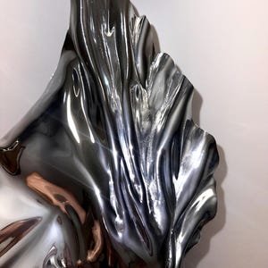 May include: A silver metal sculpture with a flowing, abstract design. The sculpture is highly reflective and has a smooth, polished finish.