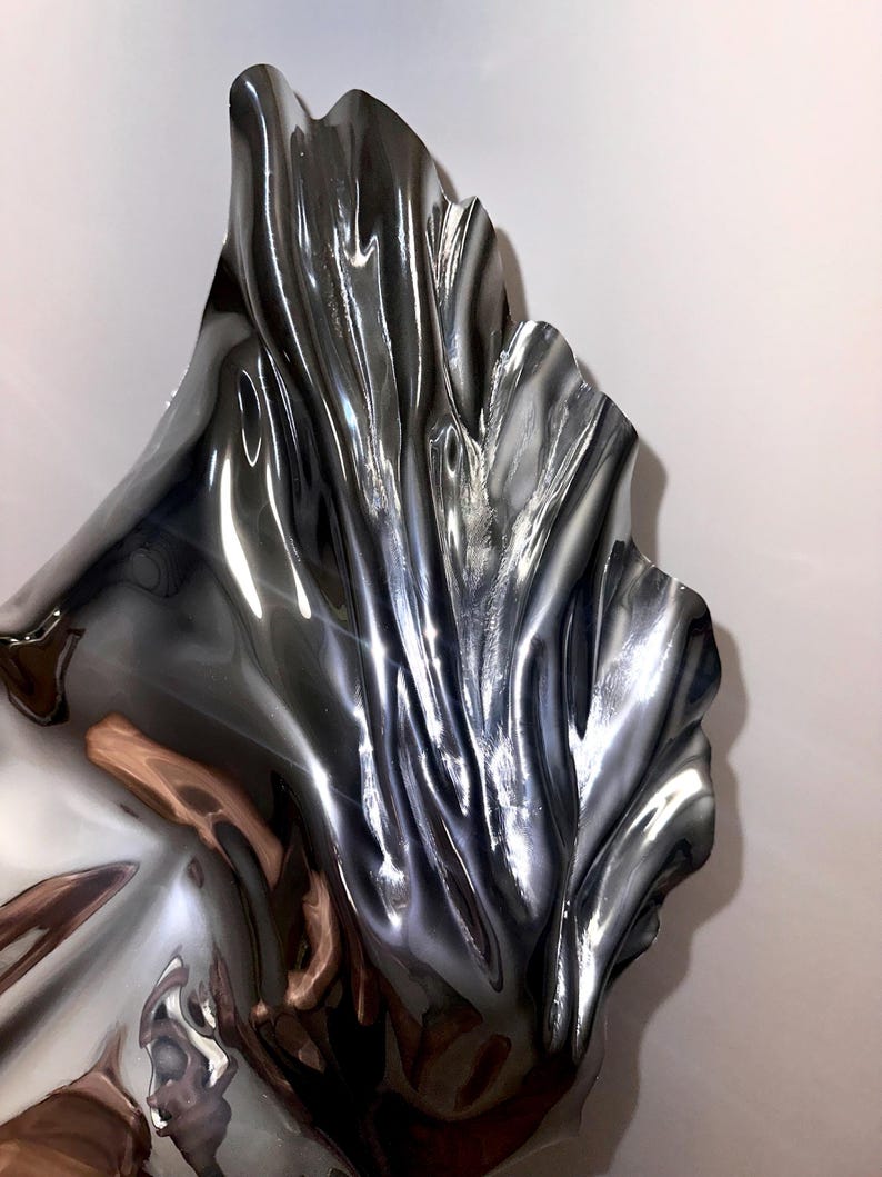 May include: A silver metal sculpture with a flowing, abstract design. The sculpture is highly reflective and has a smooth, polished finish.