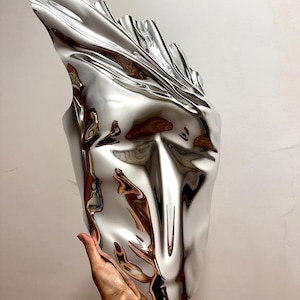 May include: A silver, abstract, face-shaped sculpture with a smooth, reflective surface.