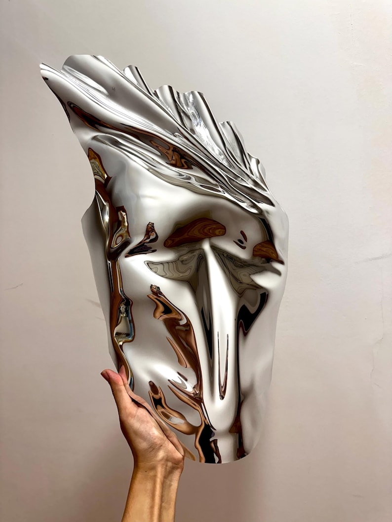 May include: A silver, abstract, face-shaped sculpture with a smooth, reflective surface.