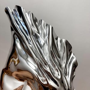 May include: A large, abstract sculpture made of polished metal. The sculpture is shaped like a flowing, draped fabric, with a smooth, reflective surface.