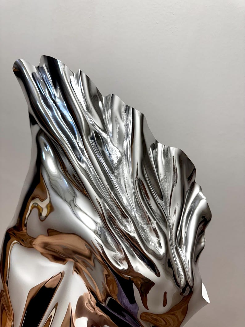 May include: A large, abstract sculpture made of polished metal. The sculpture is shaped like a flowing, draped fabric, with a smooth, reflective surface.
