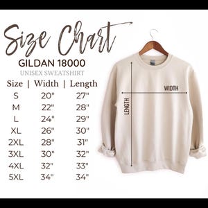 Puede incluir: Una sudadera unisex Gildan 18000 beige cuelga de una percha de madera. Se muestra una tabla de tallas, que muestra las medidas en pulgadas para las tallas S a 5XL. La tabla incluye dimensiones de ancho y largo para cada talla.
