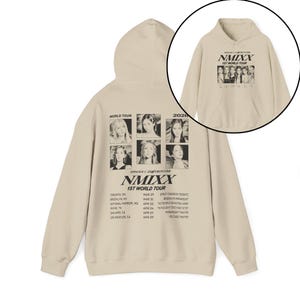 May include: Beige hoodie featuring a graphic of a group of people and the text "NMIXX 1ST WORLD TOUR 2020." The hoodie has a hood and a front pocket. The back of the hoodie has a similar graphic and tour dates.