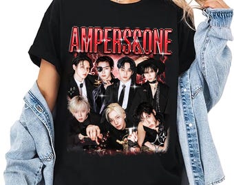 May include: Black t-shirt with the red text "AMPERS&ONE" and a graphic of a group of people in formal attire. The image shows a group of people in black suits. The t-shirt is worn by a person wearing a denim jacket.