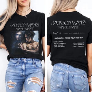 May include: Black t-shirt featuring a graphic of Jackson Wang with the text "MAGICMAN". The back of the shirt has the text "JACKSON WANG MAGICMAN" and tour dates for 2026-2027, including Los Angeles, Oakland, and Vancouver.