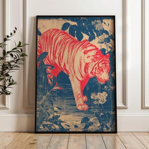 Può includere: Stampa artistica incorniciata con una tigre rossa che cammina attraverso una scena della giungla blu e beige. La tigre ha strisce rosse ed è circondata da fogliame blu e fiori bianchi. L'opera d'arte è in una cornice nera.