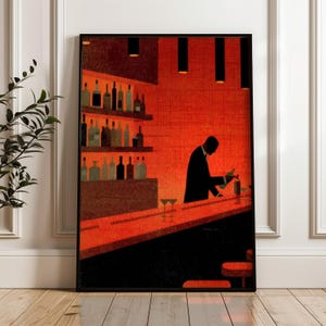Op de afbeelding: Een ingelijste kunstdruk toont een barscène in rood- en zwarttinten. Een barman in een pak schenkt een drankje achter de bar, met flessen op planken en twee martiniglazen op de toonbank. Het kunstwerk heeft een vintage, gestileerde esthetiek.