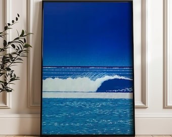 May include: A framed art print depicting a stylized ocean scene. The artwork features a deep blue sky, a white wave, and sparkling blue water. The print is in a black frame and is displayed against a white wall.