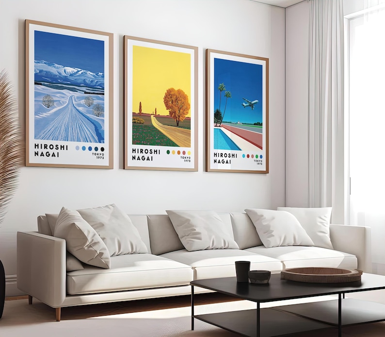 Op de afbeelding: Drie ingelijste kunstprints met een minimalistisch ontwerp. De prints tonen een besneeuwd berglandschap, een geel veld met een boom en een zwembad met een vliegtuig dat erboven vliegt. Elke print heeft de tekst "HIROSHI NAGAI" en een datum.