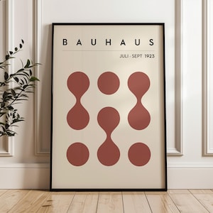Puede incluir: Un póster con el texto "BAUHHAUS JULI - SEPT 1923" en texto negro sobre un fondo crema. El póster presenta un diseño geométrico de seis círculos rojos con una forma de lágrima en el centro de cada círculo.