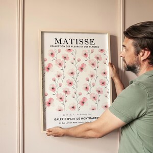 May include: A framed art print featuring a watercolor painting of pink flowers on a white background. The print has the text "MATISSE COLLECTION DES FLEURS ET DES PLANTES" at the top and "GALERIE D'ART DE MONTMARTRE 83 Rue Le Gare Nord, 75942, Paris" at the bottom.