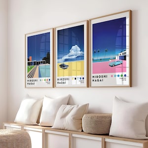 Op de afbeelding: Drie ingelijste kunstprints met een retro-esthetiek. De prints tonen een blauwe lucht, palmbomen, een auto en een huis. De prints zijn getiteld "Hiroshi Nagai" en "Tokyo 1973".