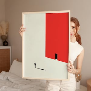 Pode incluir: Uma impressão de arte minimalista que apresenta uma silhueta preta de uma pessoa em pé em frente a uma forma retangular vermelha com uma porta preta. O fundo é de cor bege claro.