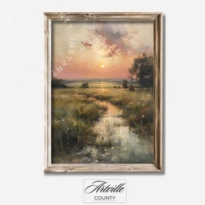 Op de afbeelding: Een ingelijst olieverfschilderij dat een zonsondergang over een veld met een klein beekje erdoorheen laat zien. De lucht is fel roze en oranje, met wolken die de kleuren reflecteren. Het veld is groen en weelderig, met wilde bloemen verspreid. Het beekje is kalm en reflecterend, met de zonsondergang die in het oppervlak wordt weerspiegeld.