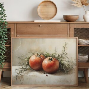 Pu&ograve; includere: Stampa incorniciata con una natura morta di due pomodori rossi maturi e rametti verdi. L'opera d'arte ha un'estetica vintage, con illuminazione soffusa e uno sfondo neutro. I pomodori sono il punto focale.