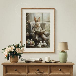 May include: A framed print depicts a rabbit in a waistcoat reading a book in a chair, surrounded by chicks and Easter eggs. The artwork has a vintage, pastel color palette, with a wooden frame. The scene evokes a cozy, springtime atmosphere.