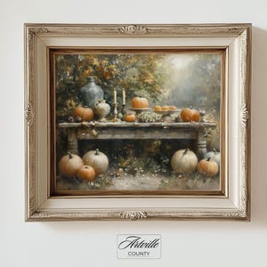 Puede incluir: Pintura enmarcada que representa una escena de cosecha otoñal. Una mesa de madera está adornada con calabazas, calabacines y velas. La obra de arte está enmarcada en un marco adornado de color crema. La pintura está firmada "Artville County".