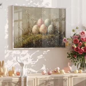 May include: A framed print featuring a still life of Easter eggs with floral patterns, set in a grassy area. The artwork is displayed above a wooden cabinet with decorative bunny figurines and a vase of pink roses. The image has the text "Arterville County".