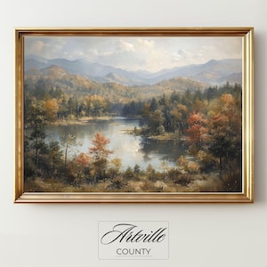 May include: A framed landscape painting of a lake surrounded by autumnal trees. The artwork, in a gold frame, features the text "Artville County" at the bottom. The painting depicts a tranquil scene with mountains in the background, evoking a sense of peace.