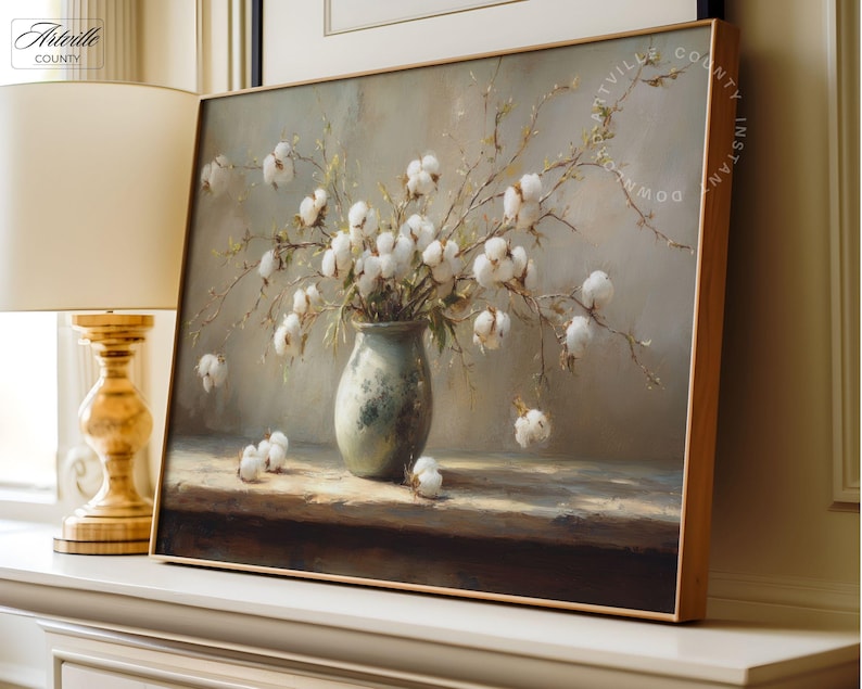 May include: A framed painting depicts a still life of cotton branches in a vase. The vase is a muted green, and the cotton bolls are white. The artwork has a soft, neutral color palette and is displayed on a white surface.