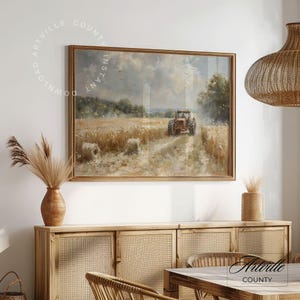 Puede incluir: Pintura de paisaje enmarcada que representa un tractor rojo en un campo de trigo. La obra de arte tiene un marco dorado y se exhibe sobre un mueble de madera. La escena se desarrolla bajo un cielo nublado, con balas de heno en primer plano.