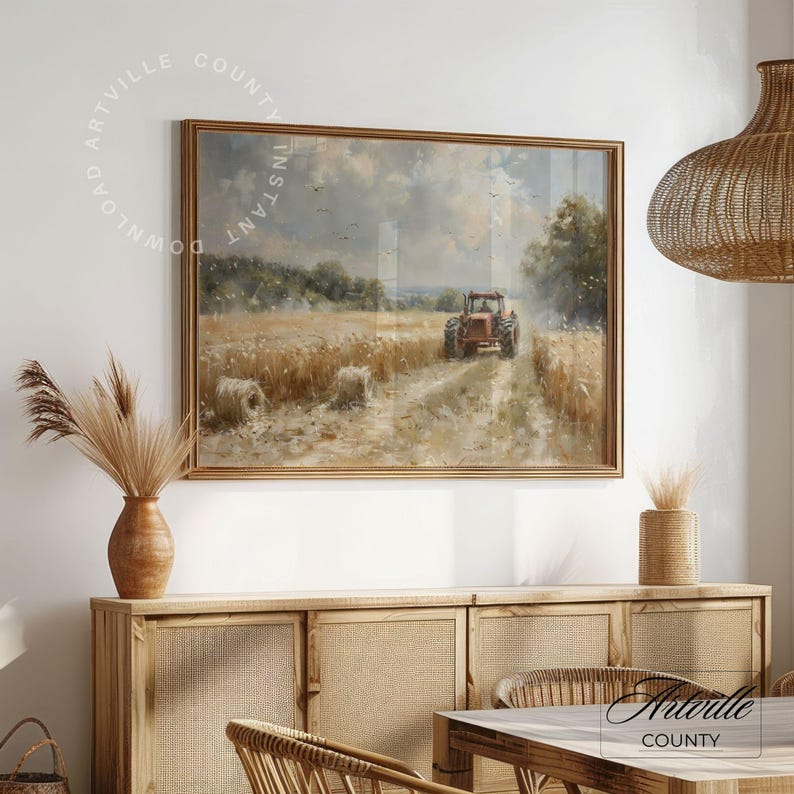 Puede incluir: Pintura de paisaje enmarcada que representa un tractor rojo en un campo de trigo. La obra de arte tiene un marco dorado y se exhibe sobre un mueble de madera. La escena se desarrolla bajo un cielo nublado, con balas de heno en primer plano.
