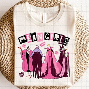 May include: A white t-shirt with the text "MEAN GIRLS" in black letters with pink accents. The shirt features a graphic of four Disney villains: Ursula, Maleficent, Cruella de Vil, and the Evil Queen.