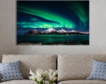 Könnte beinhalten: Leinwanddruck einer Landschaft mit Nordlichtern. Das Bild zeigt eine lebendige Darstellung von grünen und türkisfarbenen Polarlichtern über schneebedeckten Bergen und einem dunkelblauen Gewässer.