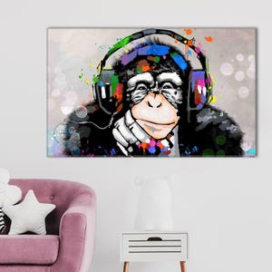 May include: A colorful pop art canvas print featuring a chimpanzee wearing headphones. The chimpanzee is depicted with a white face, black fur, and colorful paint splatters. The headphones are also decorated with vibrant colors.