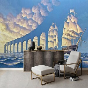 Puede incluir: Un dise&ntilde;o de interior de sala de estar con un sill&oacute;n y un reposapi&eacute;s blancos, un gabinete de madera oscura y un mural de pared que representa una escena surrealista de barcos navegando bajo un puente en un cielo nublado.