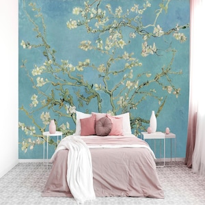 Puede incluir: Un dormitorio con un mural de la pintura "Almendros en flor" de Van Gogh. El mural es de un azul vibrante con ramas de flores blancas. La cama tiene ropa de cama rosa, almohadas y una manta blanca.
