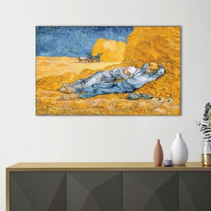 May include: A framed print of Van Gogh's "The Siesta" featuring two figures in blue and white clothing resting on a bed of hay. The artwork depicts a sunny field with haystacks and a blue sky, evoking a sense of tranquility.