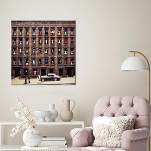May include: A vintage photograph of a city building with multiple windows. People are standing in the windows, each wearing a different coloured dress. A black car is parked in front of the building.