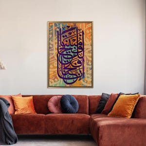 Puede incluir: Una impresi&oacute;n enmarcada de caligraf&iacute;a isl&aacute;mica en morado y azul sobre un fondo texturizado con tonos de naranja y amarillo. La caligraf&iacute;a es de estilo tradicional y est&aacute; rodeada de un marco dorado.