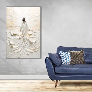 Puede incluir: Una obra de arte en lienzo blanco texturizado representa una figura con una túnica blanca caminando sobre el agua, con un fondo brillante y lleno de luz. La obra de arte se exhibe en una pared sobre un sofá azul con cojines decorativos.