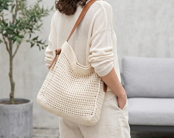 Könnte beinhalten: Eine cremefarbene, offen gewebte Tragetasche mit braunen Lederriemen wird über der Schulter getragen. Die Tasche wird mit einem cremefarbenen Pullover und Shorts kombiniert. Ein Topfpflanzenbaum und ein graues Outdoor-Sofa befinden sich im Hintergrund.