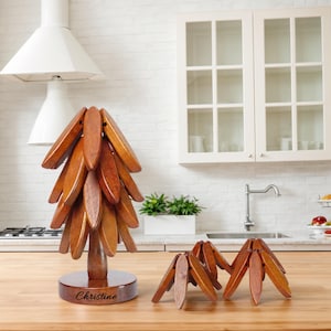 Może przedstawiać: Drewniany podkładka pod gorące w kształcie drzewa z wygrawerowanym imieniem "Christine" na podstawie. Podkładka składa się z wielu drewnianych elementów, które można składać i rozkładać. Na zdjęciu widoczne są również dwa mniejsze podkładki.