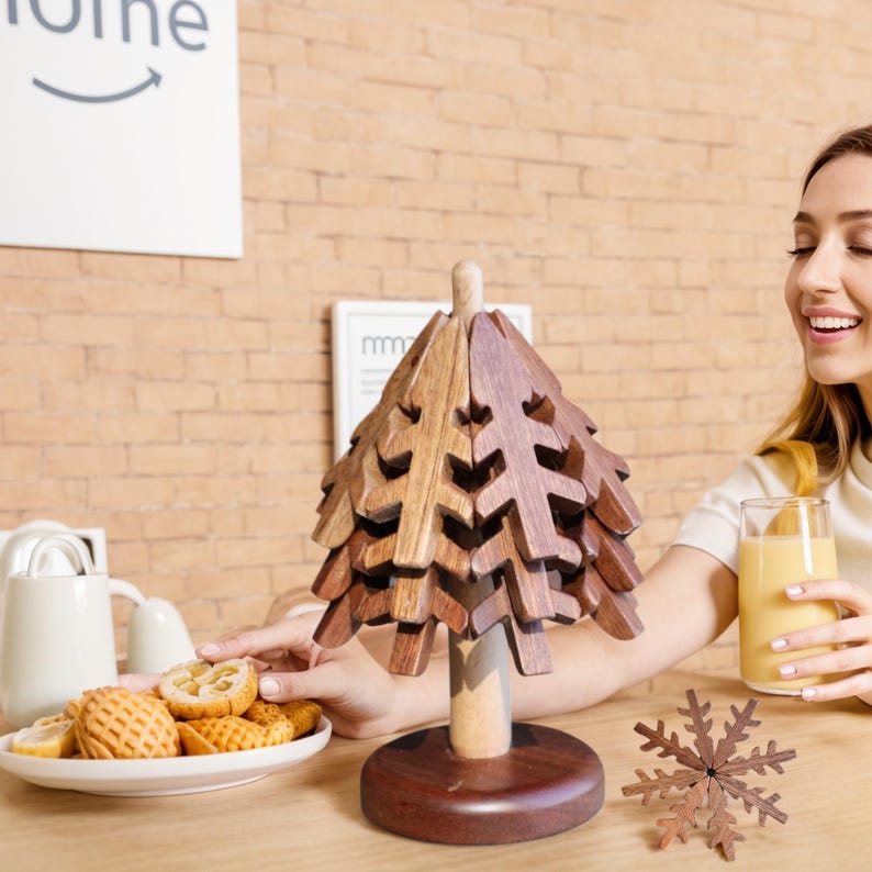 May include: A wooden Christmas tree ornament with a brown and natural wood finish. The tree is made of interlocking pieces that can be stacked to create a unique and decorative piece. The tree is sitting on a table with a plate of biscuits and a glass of juice.
