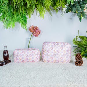 May include: Two pink and white cosmetic bags with a repeating Mickey Mouse pattern. The bags are rectangular and have a checkered background. A Coca-Cola bottle is visible on the left side of the image.