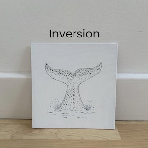 May include: A square white canvas featuring a black ink stippled illustration of a whale tail emerging from water. The word Inversion is printed in black text above the artwork. The design uses dot work to create texture and shading on the tail.