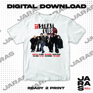 May include: White t-shirt featuring a graphic of the K-pop group Stray Kids. The group members are wearing black clothing and are standing in a line. The text "SKZ STRAY KIDS" is printed in red and black on the shirt. The names of the group members are listed below the graphic.