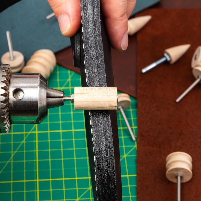 Puede incluir: Primer plano de un proyecto de artesan&iacute;a en cuero que se est&aacute; trabajando con un taladro y una clavija de madera. El cuero es negro y tiene costuras alrededor del borde. La clavija se est&aacute; insertando en el cuero con el taladro.